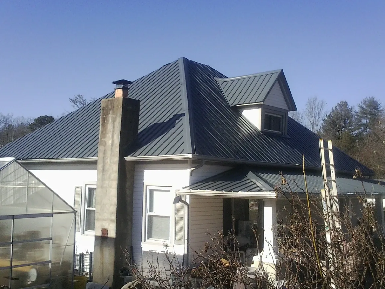 Dark blue standing seam metal roof on a white farmhouse with dormer — Slate & Tile Roof Repair by Roofing Brothers in Follansbee