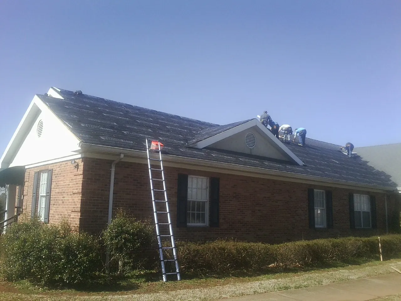 Crew tearing shingles off a brick ranch roof with a ladder set — Metal Roof Repair work by our crew in Follansbee