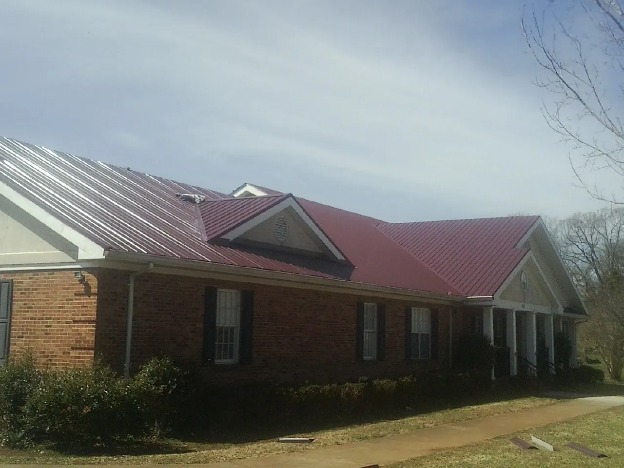 Red metal roof with gabled entries on a long brick building, from a Hail Damage Roof Repair job in Follansbee