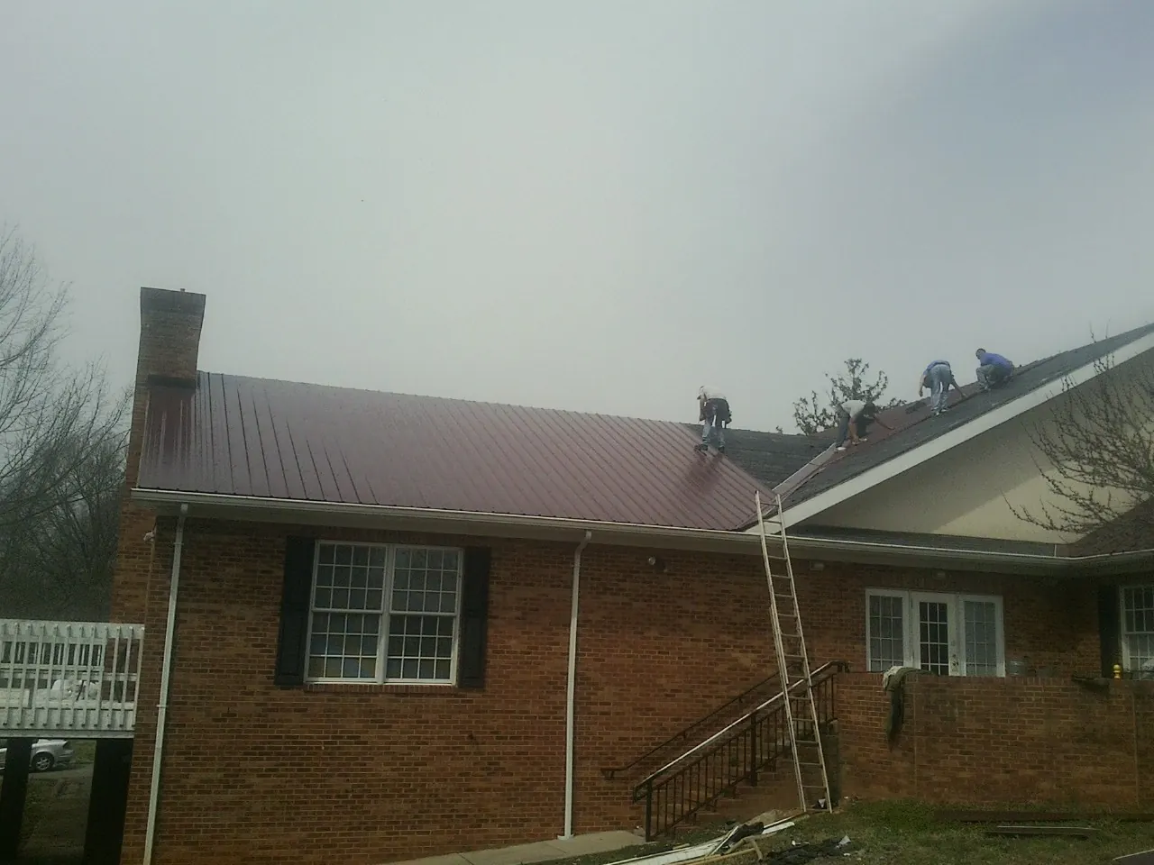 Crew setting red metal roofing panels on a brick home in Follansbee