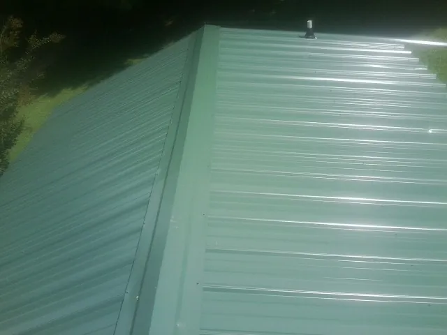 New green metal panels meeting at the ridge of a roof — Flat Roof Repair work by our crew in Follansbee