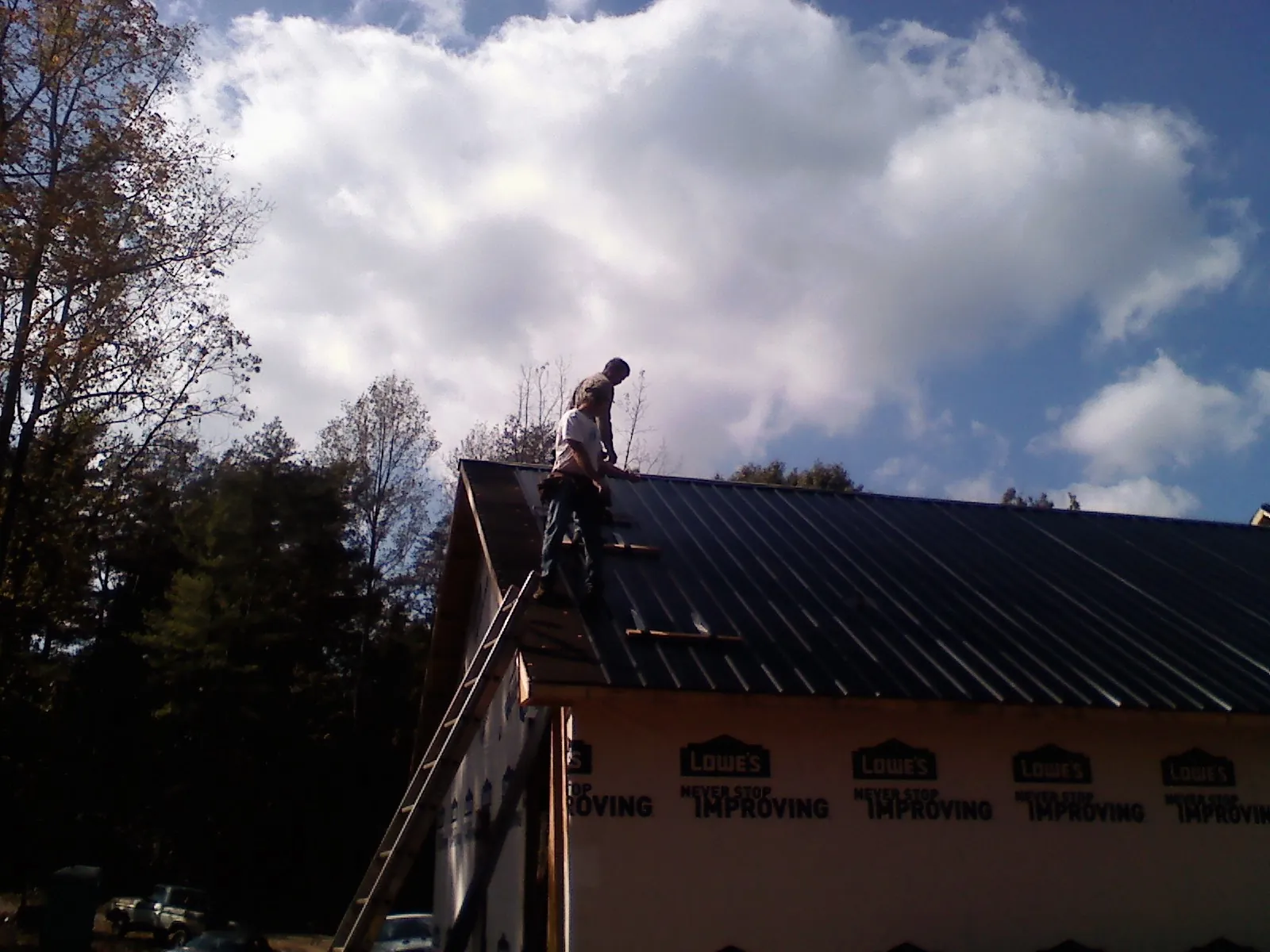 Roofer fastening dark metal panels high against a cloudy sky, from a Roof Inspection job in Follansbee