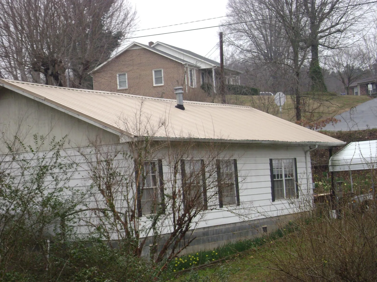 Tan metal roof on a white sided house set into a hillside — Commercial Roofing by Roofing Brothers in Follansbee