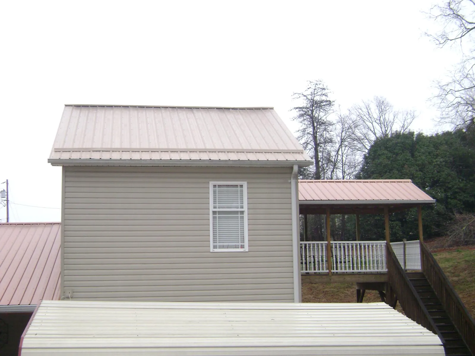 Tan metal roofs on a two story addition and attached porch, from a Roof Replacement job in Follansbee